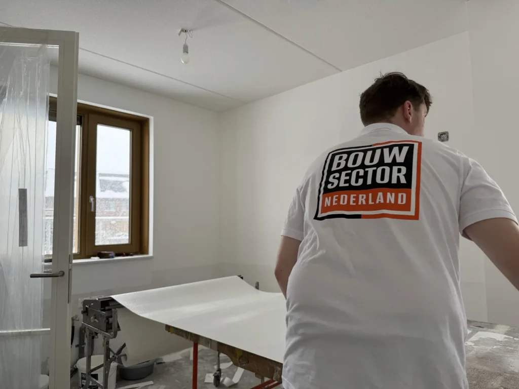 Behanger van Bouwsector Nederland rolt een baan behang uit over de plaktafel