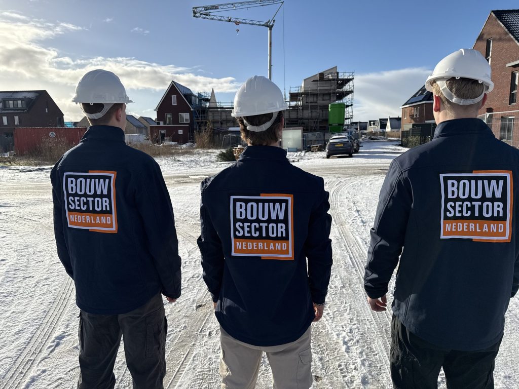 Drie vakmensen van Bouwsector Nederland met witte bouwhelm kijken naar woningen in aanbouw
